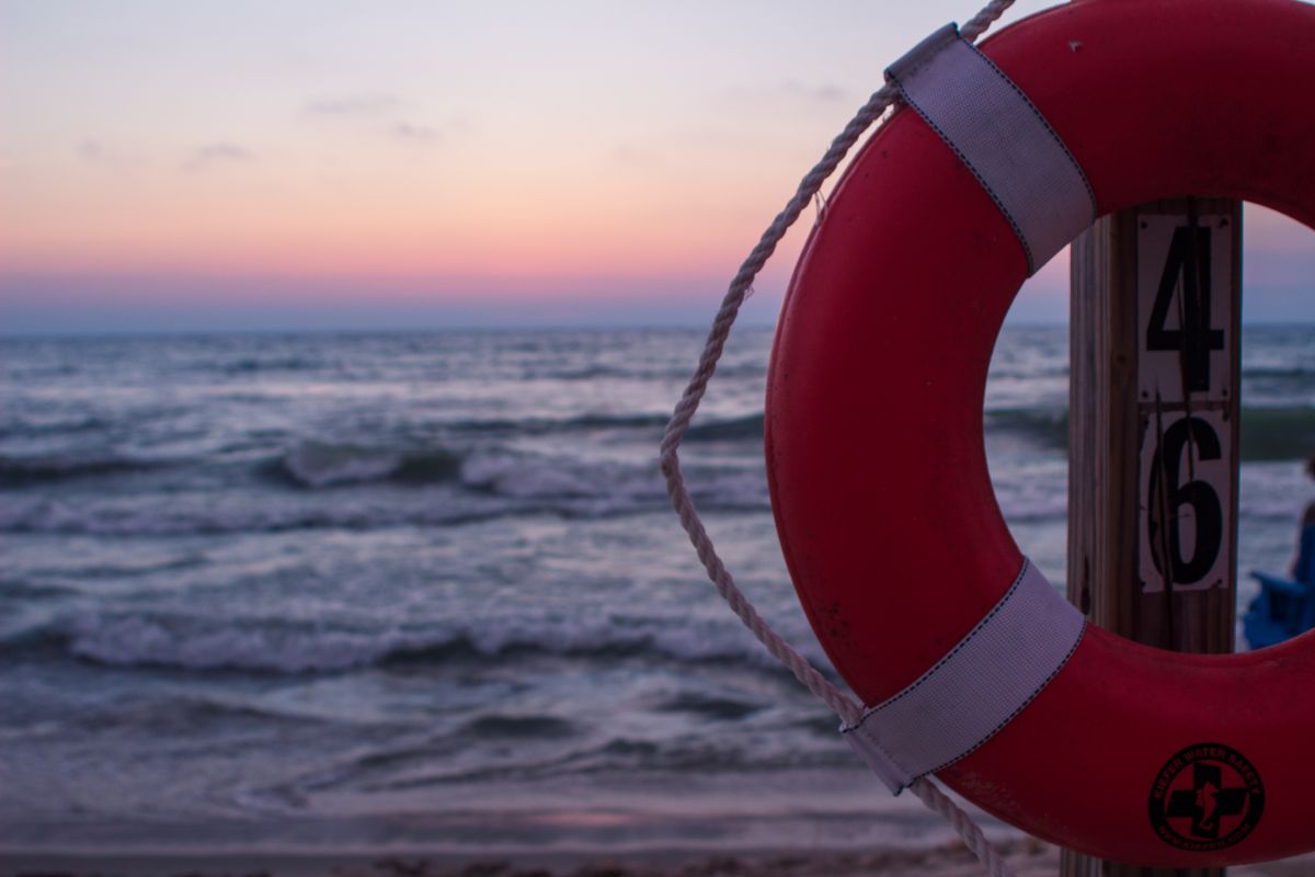 A photo by Jared Berg showing a life preserver in the foreground with a sunset over the sea in the background