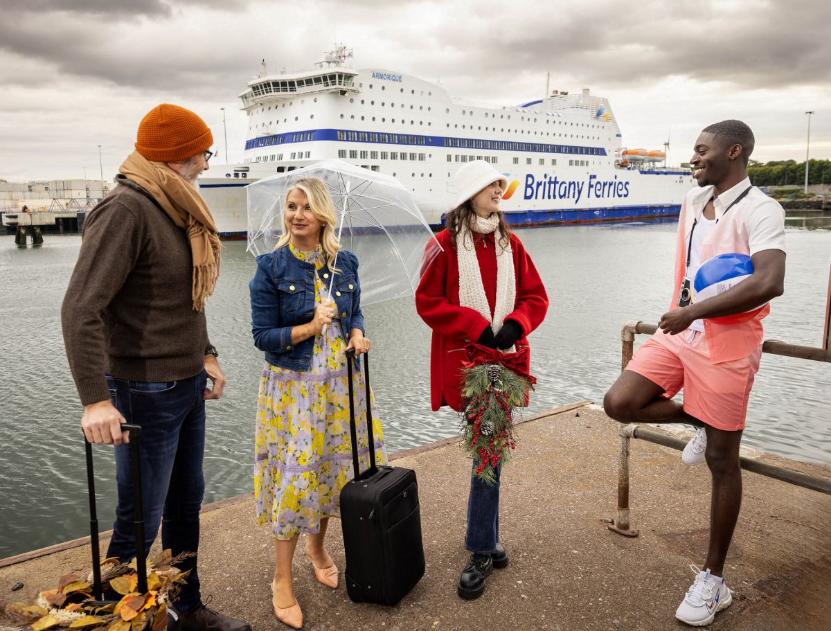 Four individuals dressed in various holiday outfits stand before a Brittany Ferries vessel
