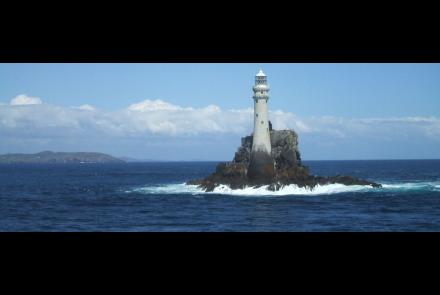 Fastnet Rock Lighthouse standing on a small rocky island surrounded by the ocean, with distant land visible on the horizon.